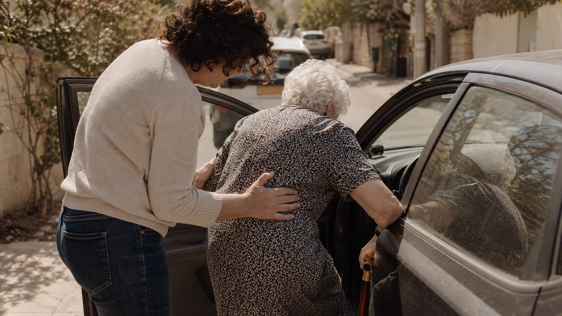 אדם מבוגר עם מקל הליכה נעזר ביד תומכת להיכנס לרכב - זכאות לתג נכה